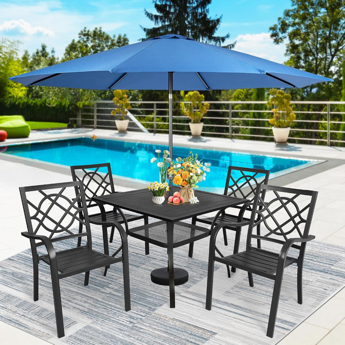 Black square table and four chairs under a large blue patio umbrella with a swimming pool in the background