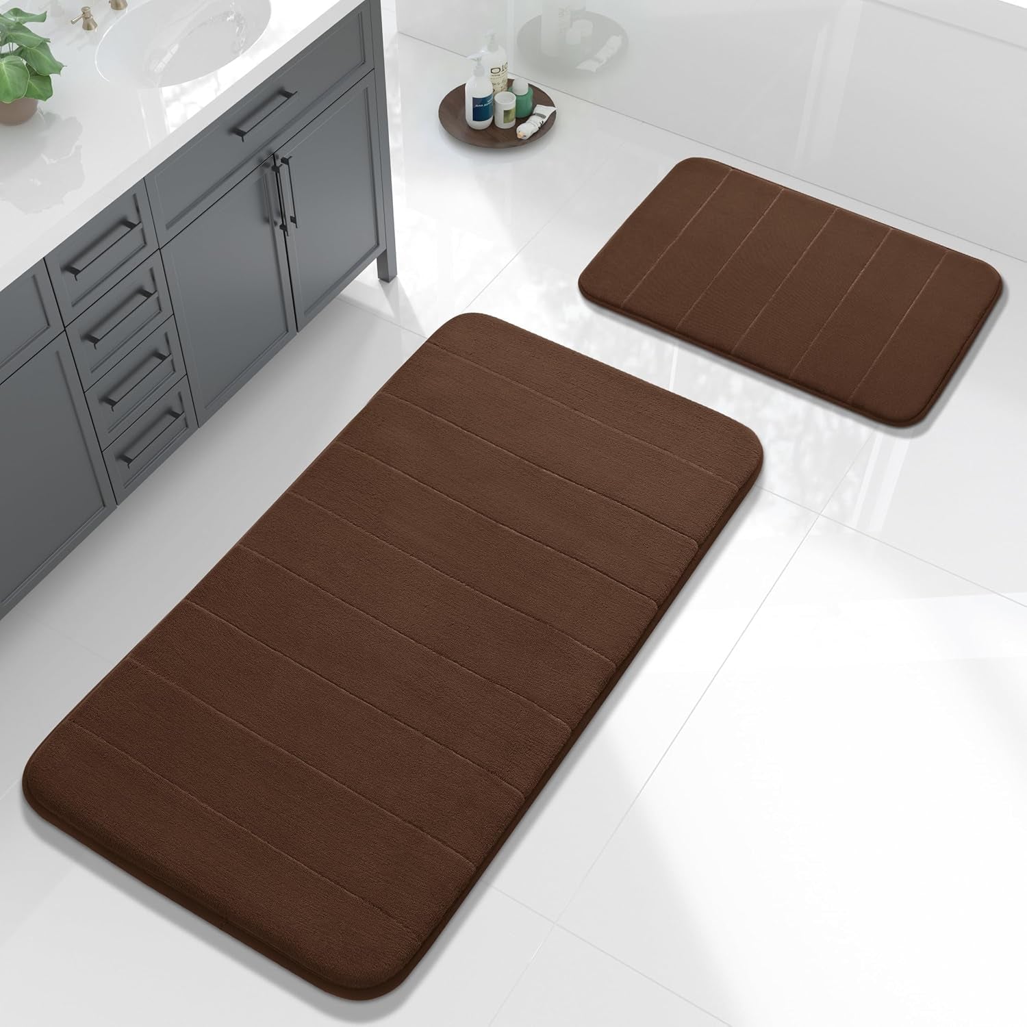 Overhead shot of two brown bath mats on glossy white tile beside a gray vanity