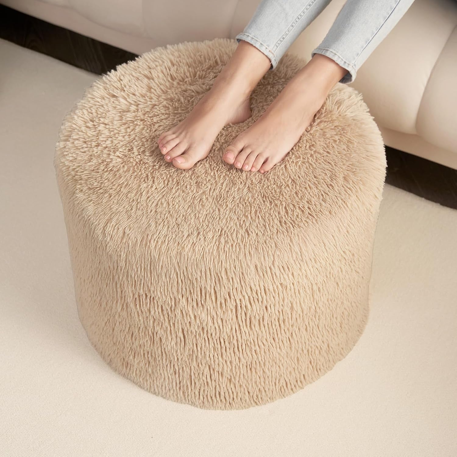 Close-up top view of a tan round pouf with a pair of bare feet resting on the fuzzy surface.