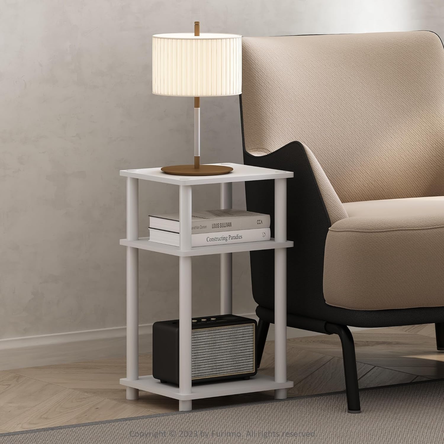 White three-tier side table next to an upholstered chair with a lamp and stacked books.