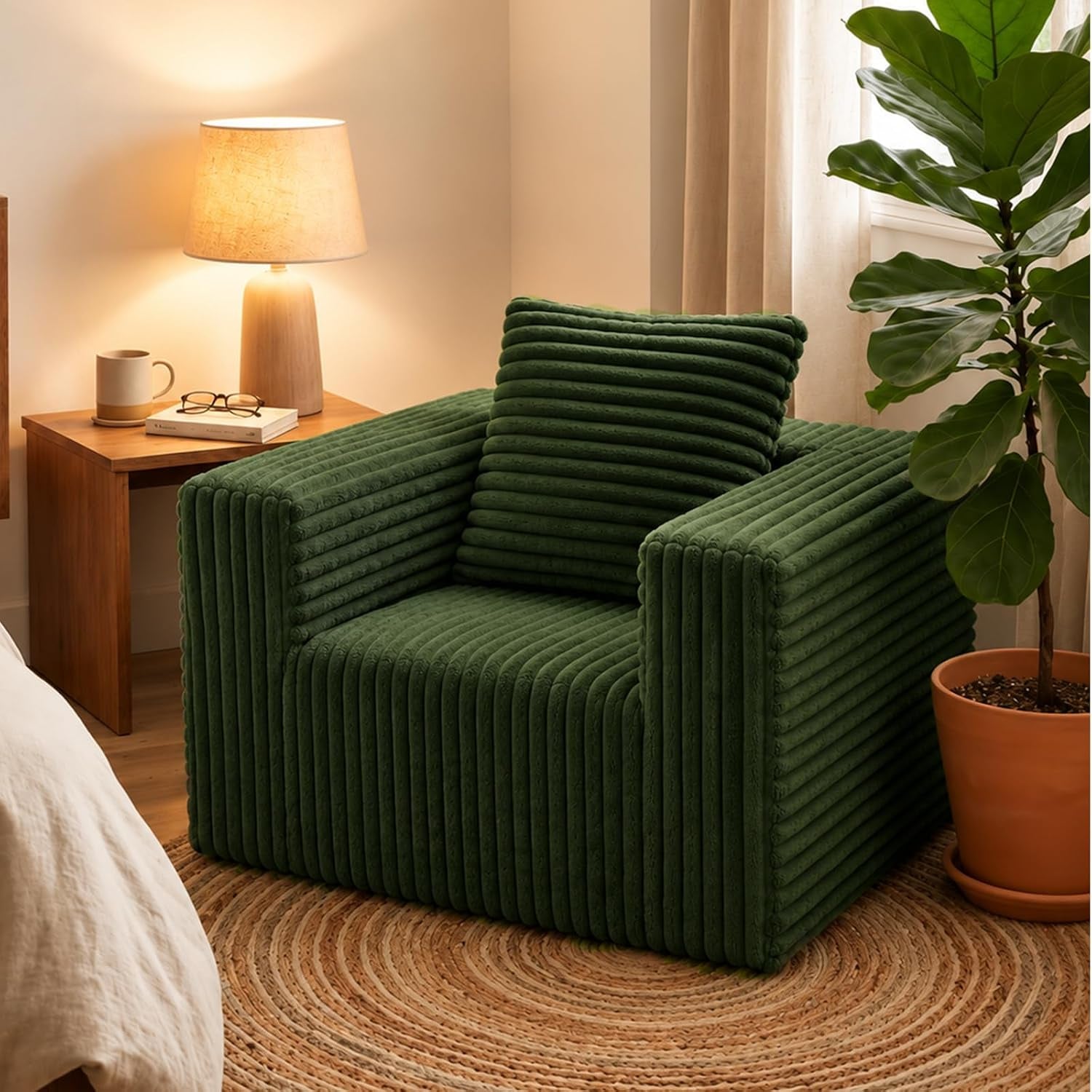 Green corduroy floor chair with matching square cushion on a round woven rug beside a nightstand and potted plant.