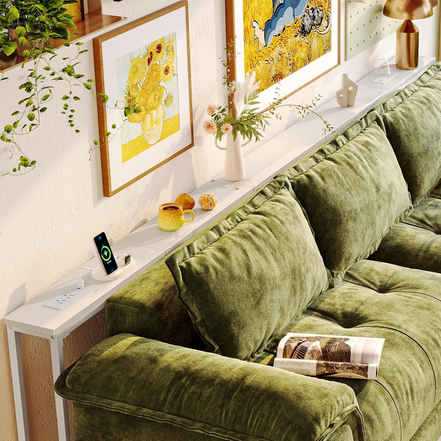 White skinny console table behind a green sectional with vase, phone charger, and framed art above