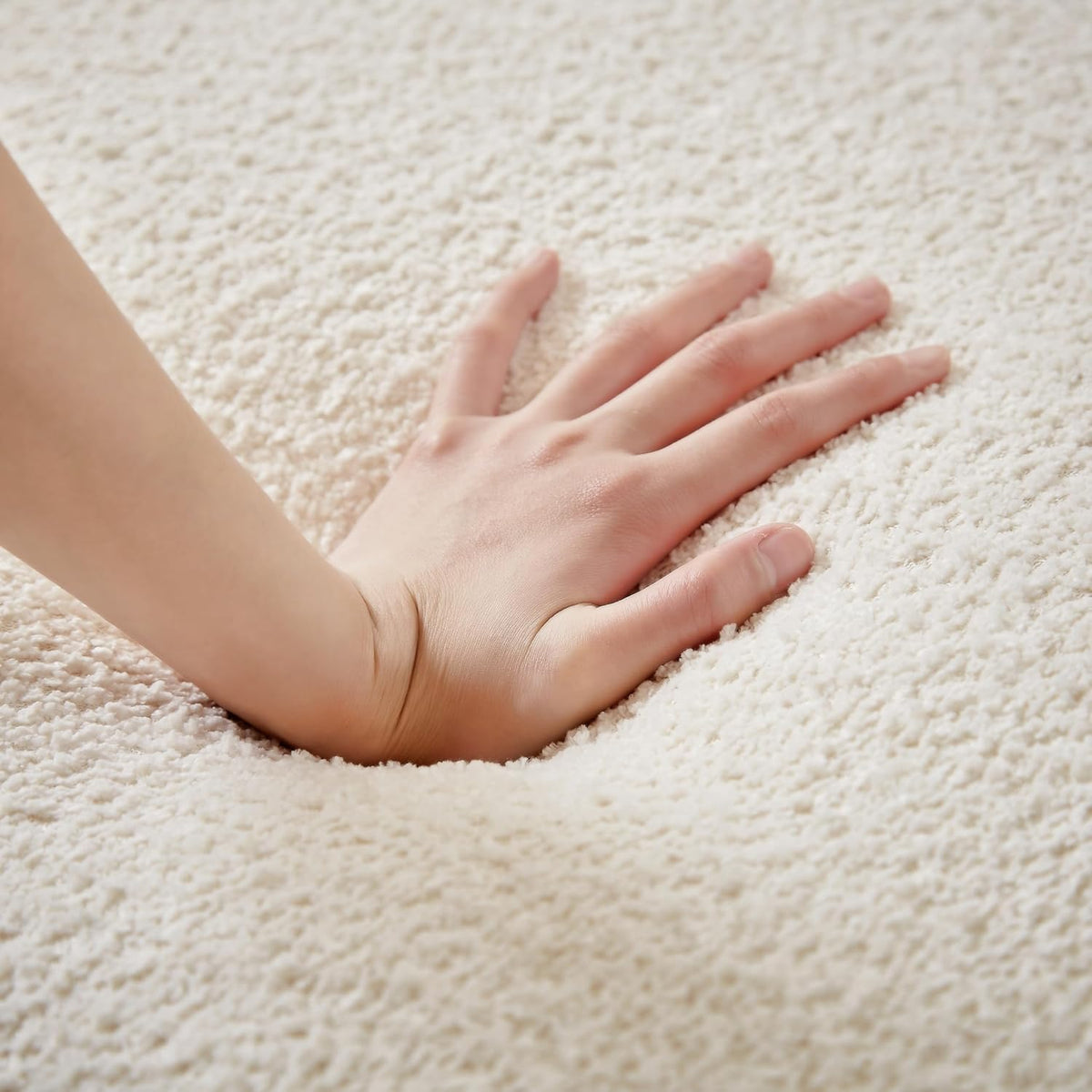 Close-up of a hand pressing cream boucle-like upholstery showing foam indentation