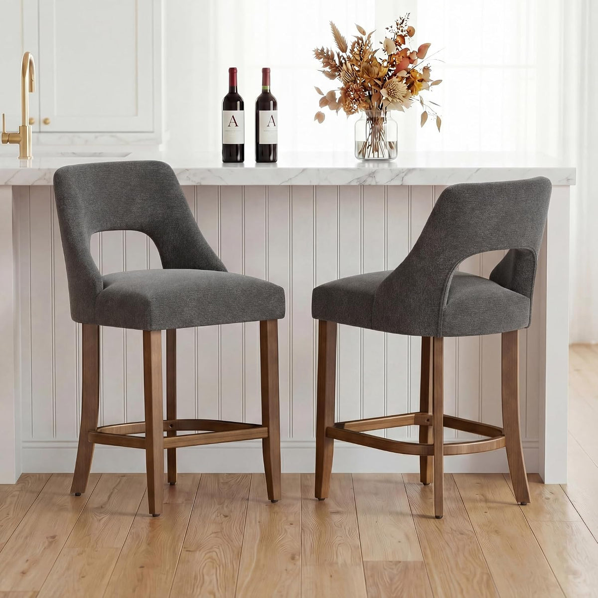 Two charcoal-upholstered counter stools with wood legs tucked at a white kitchen island.