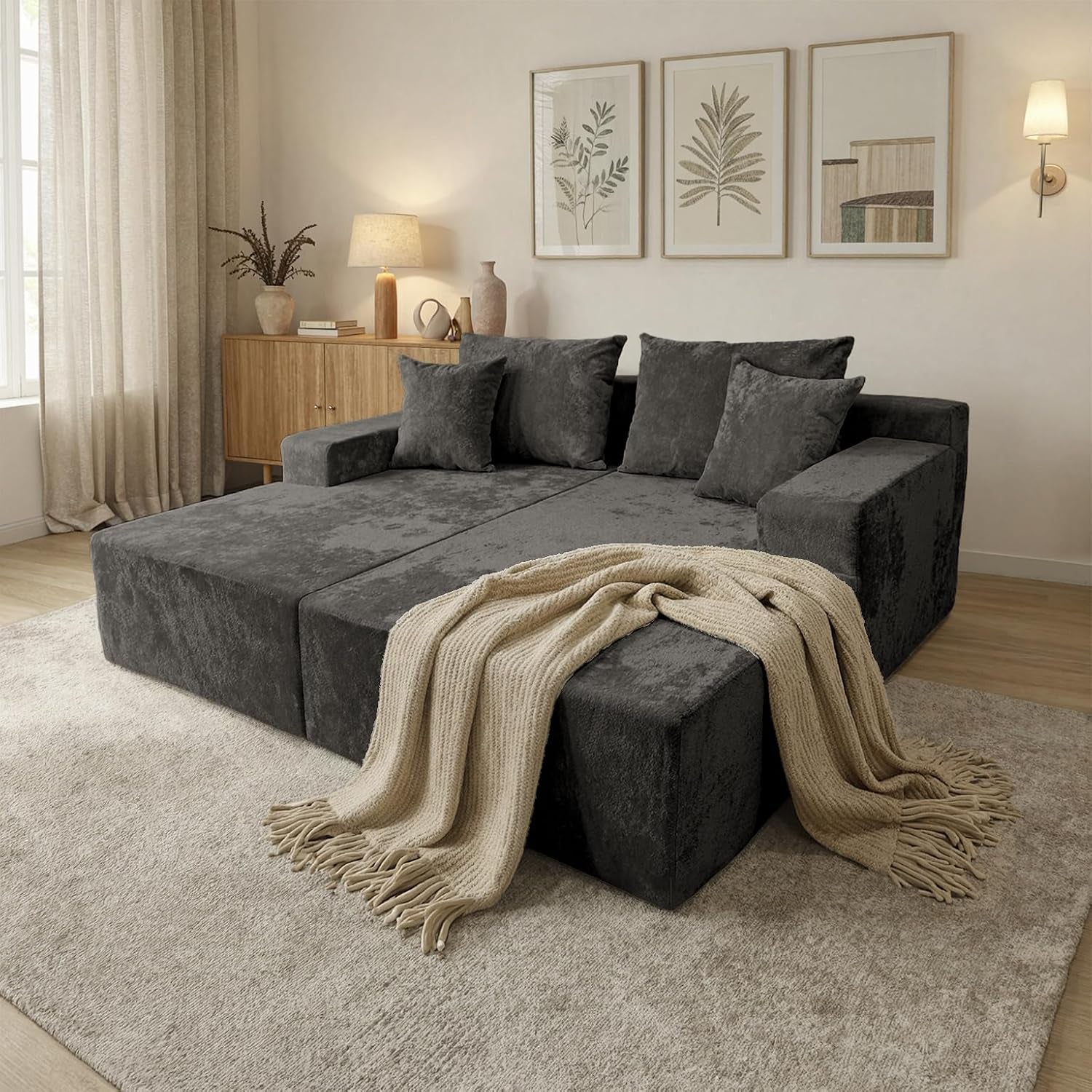 Three-quarter view of the dark-gray two-seat floor sleeper laid flat with four back cushions and a beige knit throw.