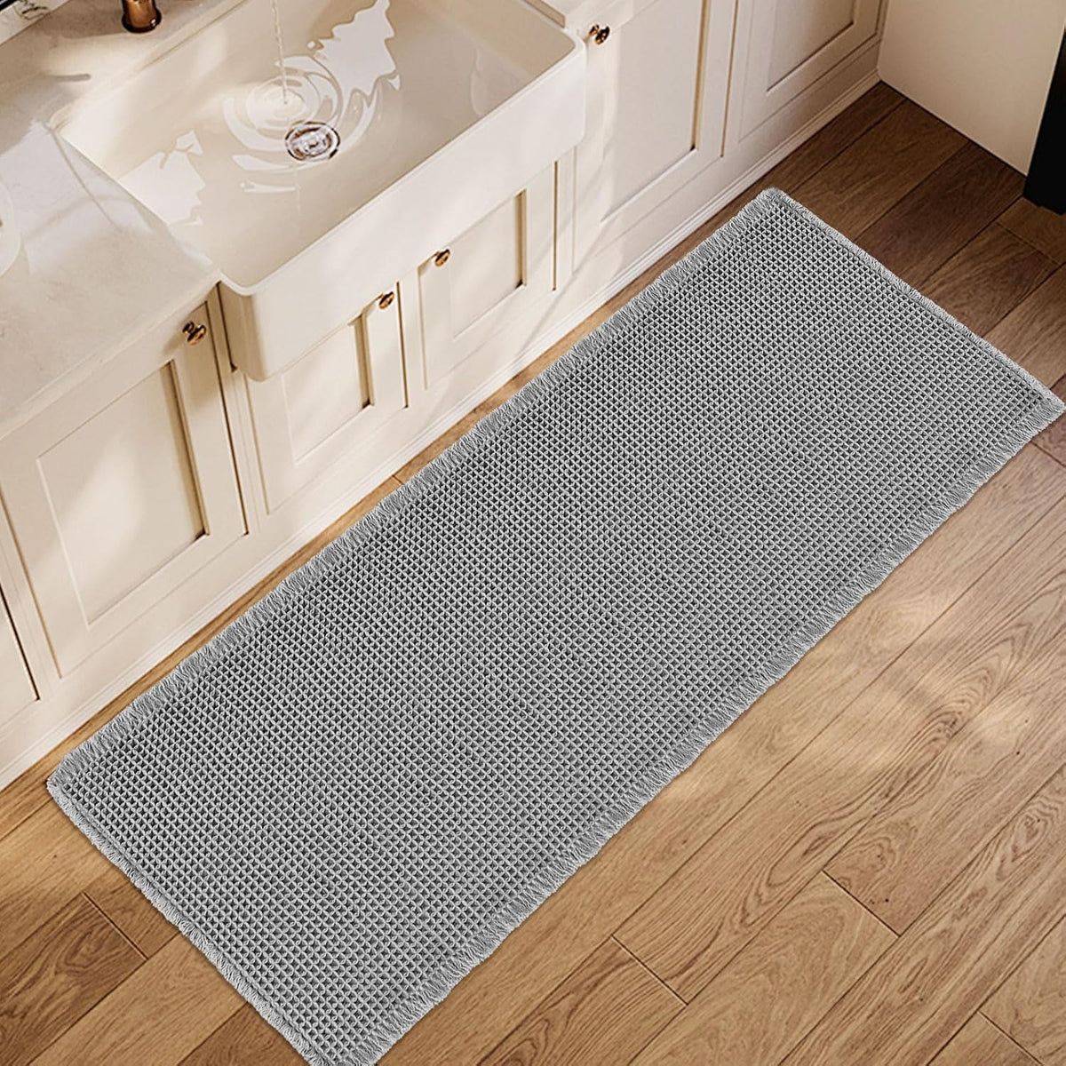 Top-down view of a long light-gray waffle runner placed by a white sink on wood flooring.