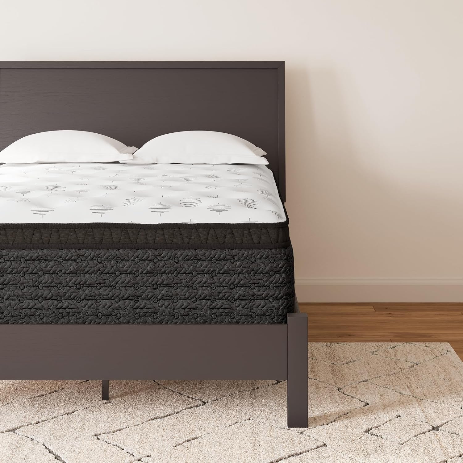 Close front view of a mattress with white quilted top and dark gray textured sides on a low wood bed frame.