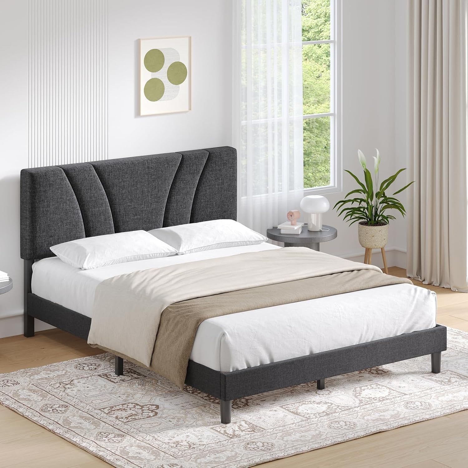Angled bright-room view of a charcoal upholstered platform bed with white bedding.