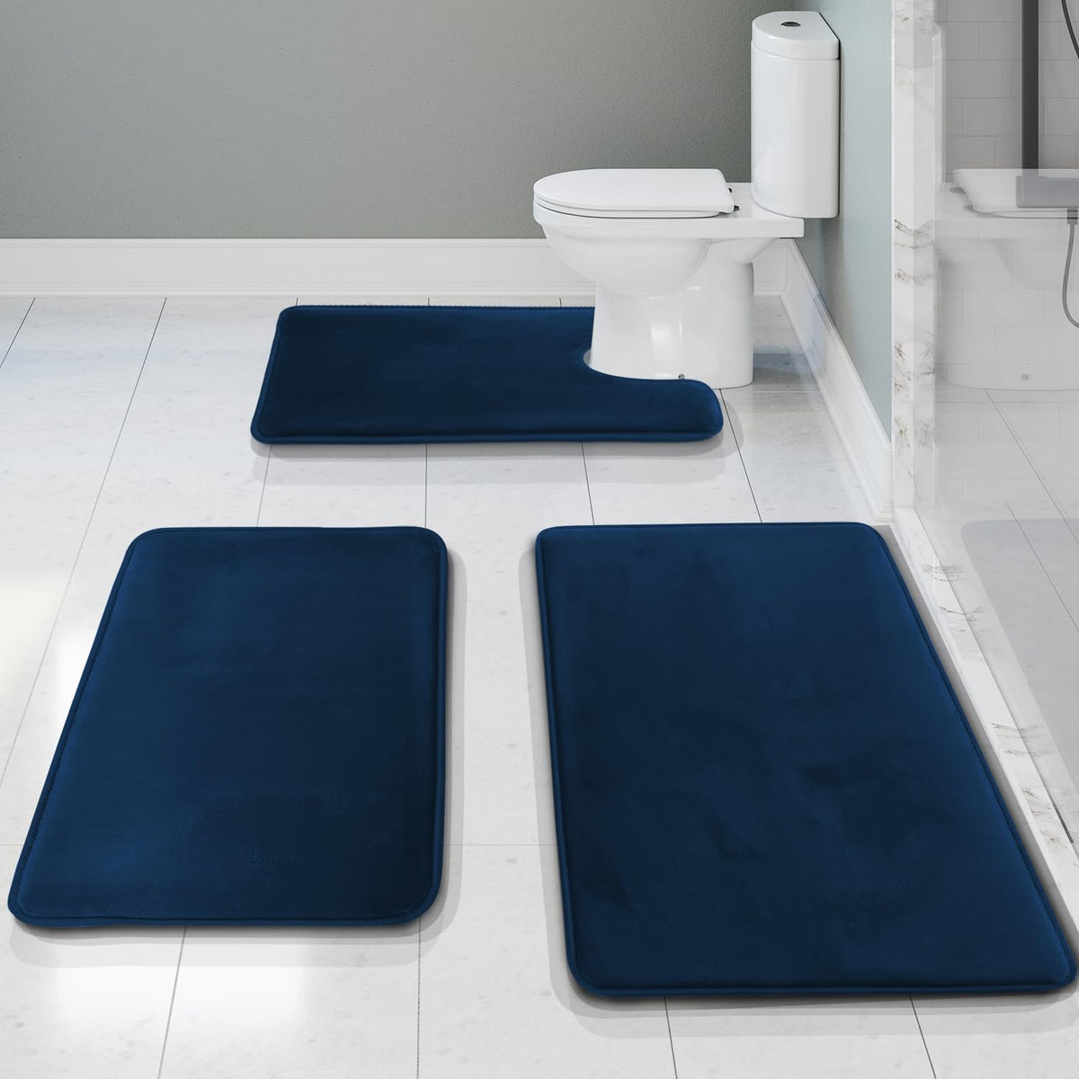 Overhead bathroom view showing three navy-blue memory foam rugs, including a U-shaped rug positioned at the toilet.