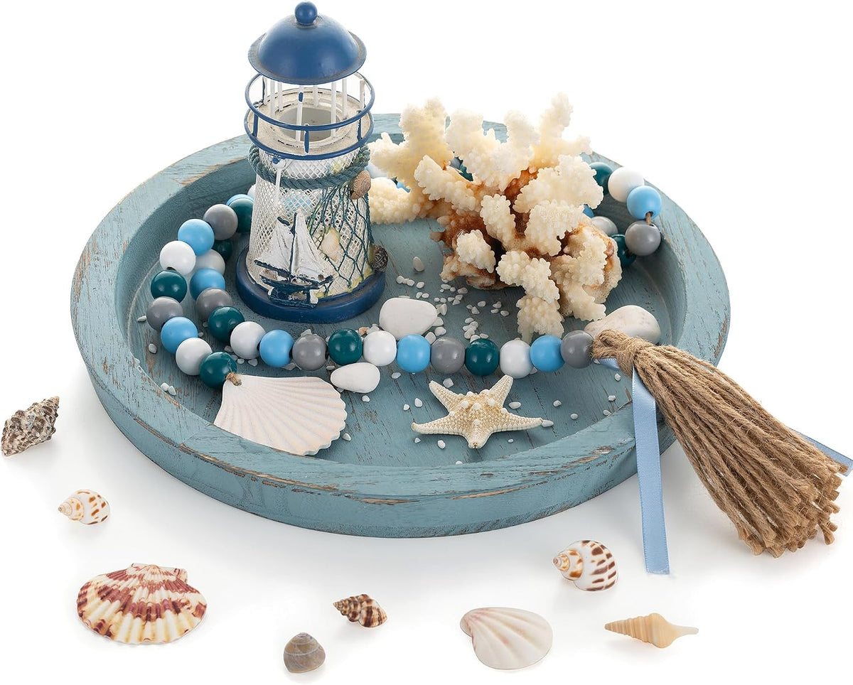 Round distressed blue wooden tray filled with seashells, coral, beads and a miniature lighthouse