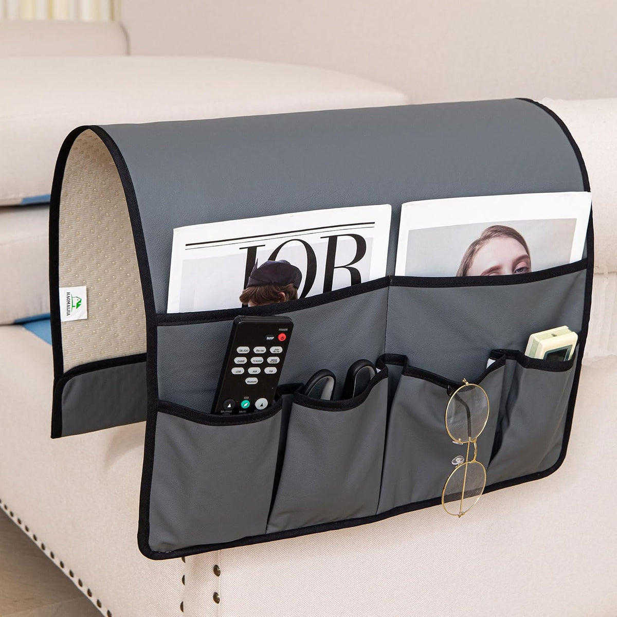 Dark gray armrest caddy draped over a beige sofa arm with magazines and small items in pockets.