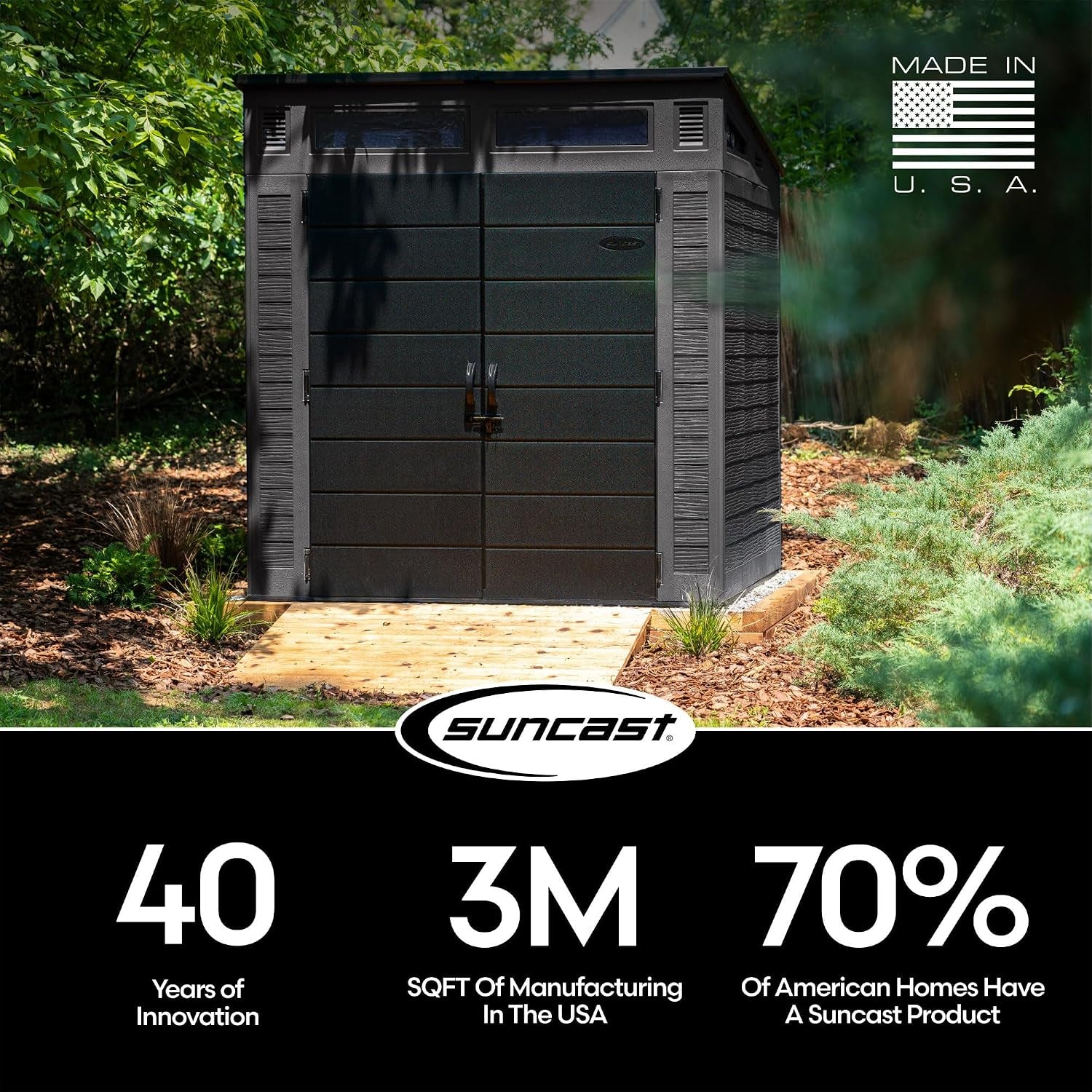 Front view of a dark peppercorn resin outdoor storage shed with double doors on a small wooden pad in a leafy yard.