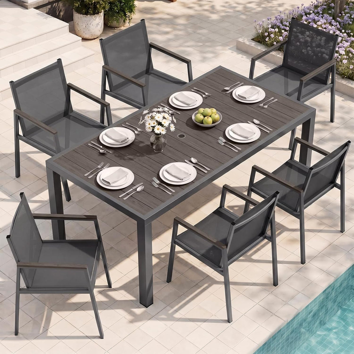 Rectangular outdoor dining table set beside a pool with six dark gray mesh chairs and place settings.
