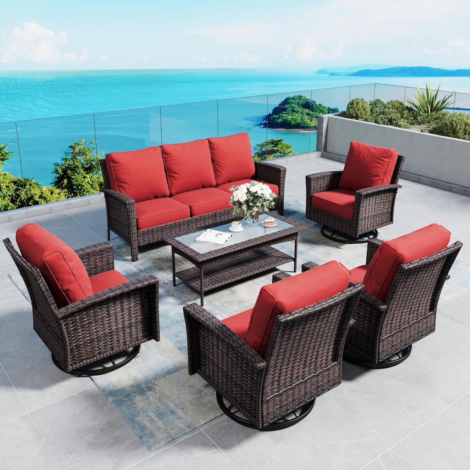 Outdoor patio set with brown wicker sofa and four swivel chairs with red cushions around a coffee table, ocean view.