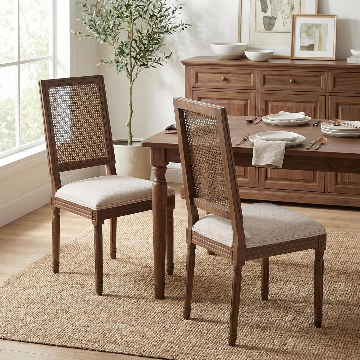 Pair of cane-back dining chairs with beige seats placed by a wood dining table and buffet in a bright dining room