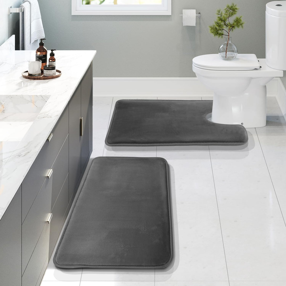 Bathroom scene with two dark gray rectangular mats and a U-shaped mat placed by a vanity and toilet on pale tiled floor.