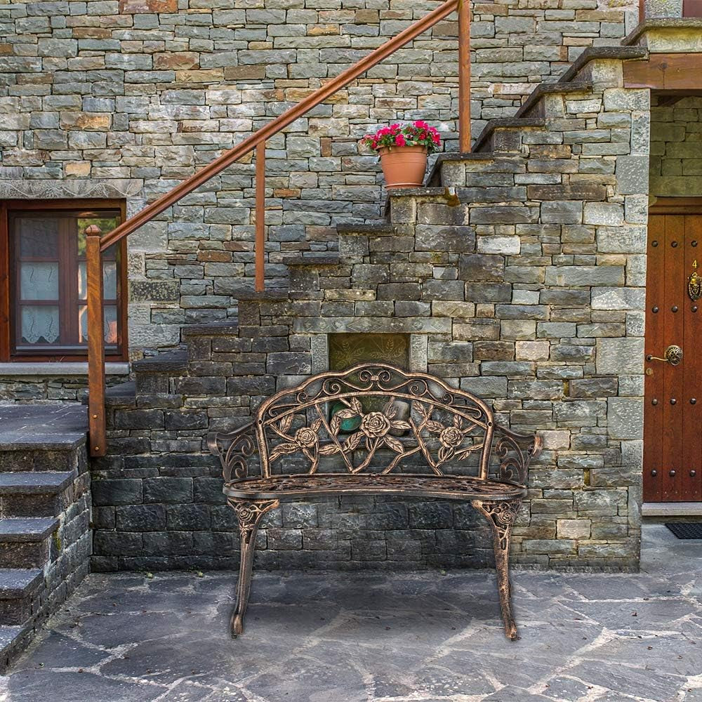 Metal rose-pattern bench staged on a stone patio in front of a stepped stone wall and wooden door