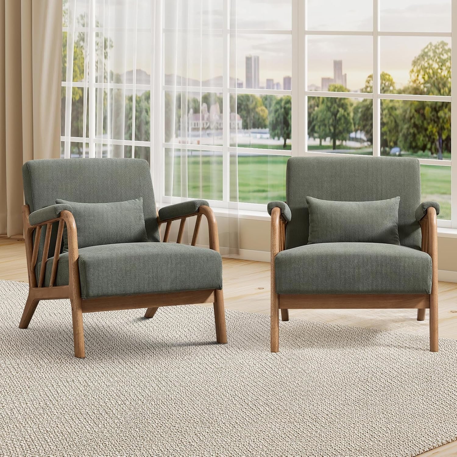 Two muted green fabric accent chairs with exposed wood arms and legs beside a bright window.