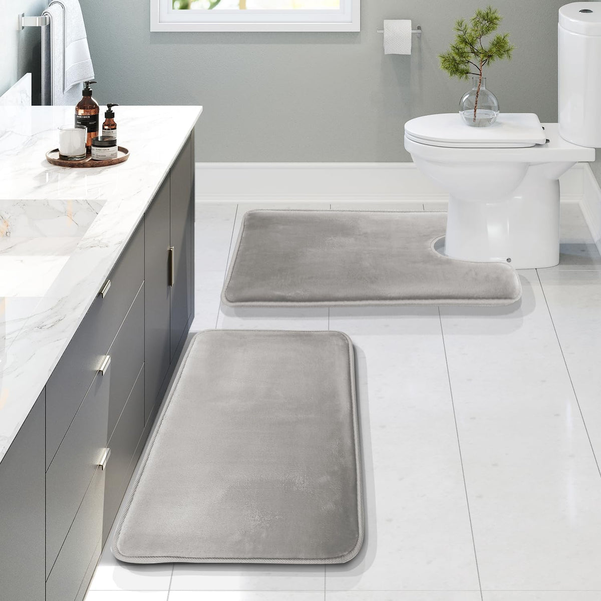 Angled shot from the vanity showing the gray U-shaped contour mat by the toilet and two rectangular mats leading toward the