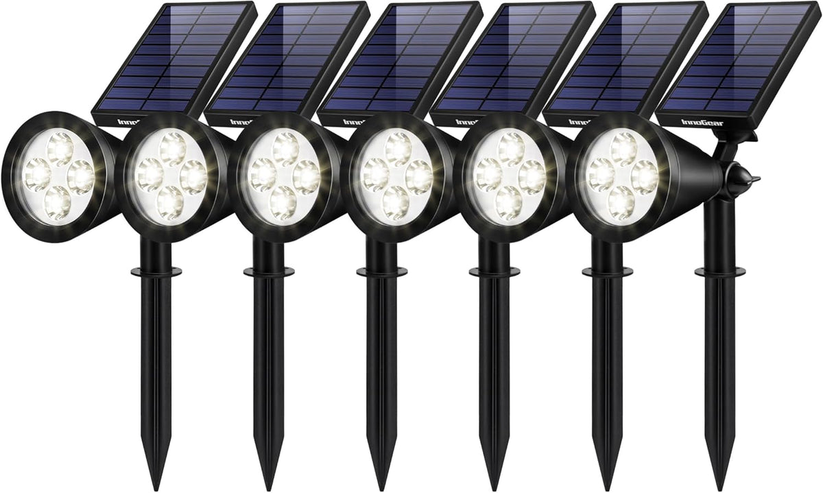 Front view of six black solar garden spotlights on stakes with angled panels and lit LED heads.