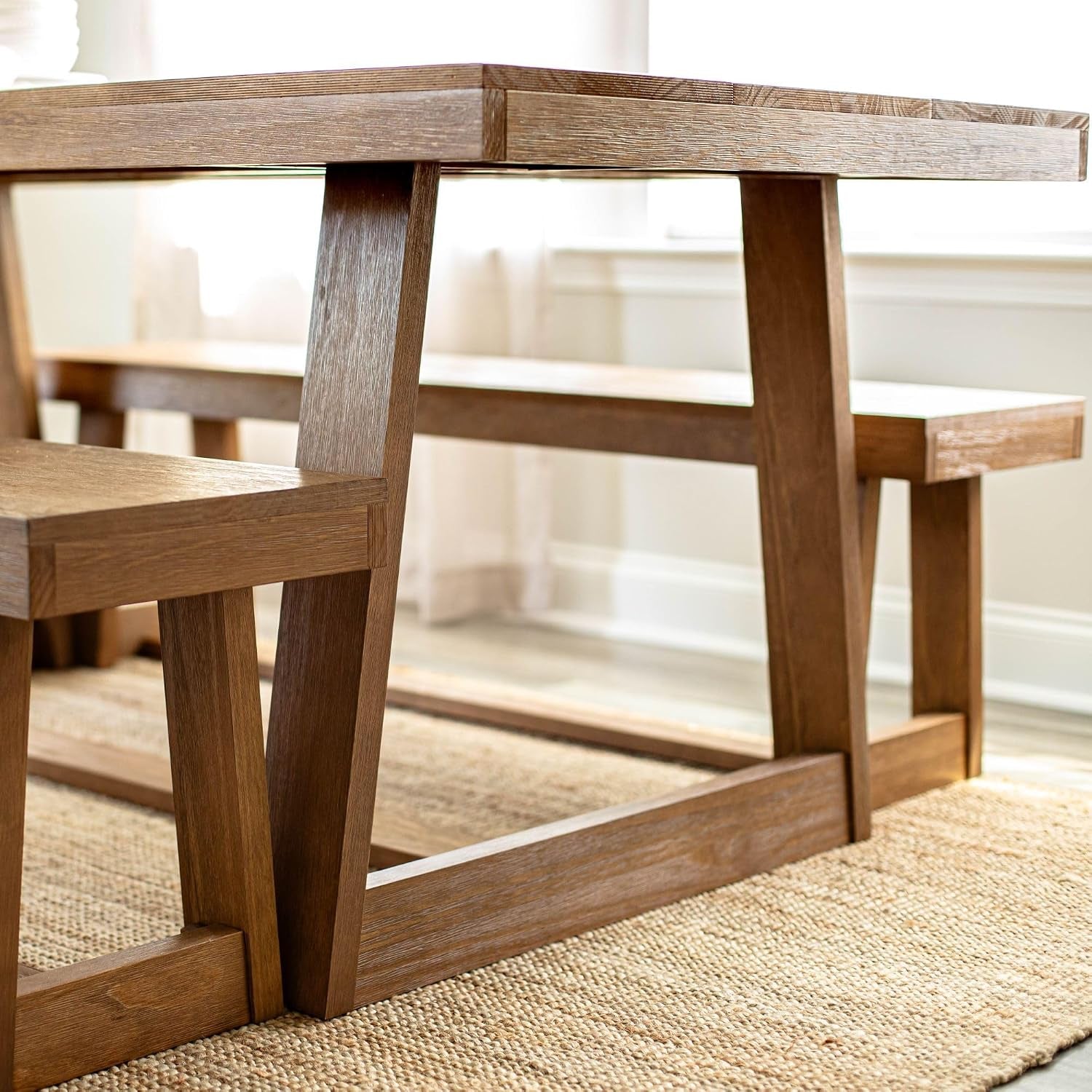 Close lifestyle view of the table base and matching bench on a woven rug near a bright window