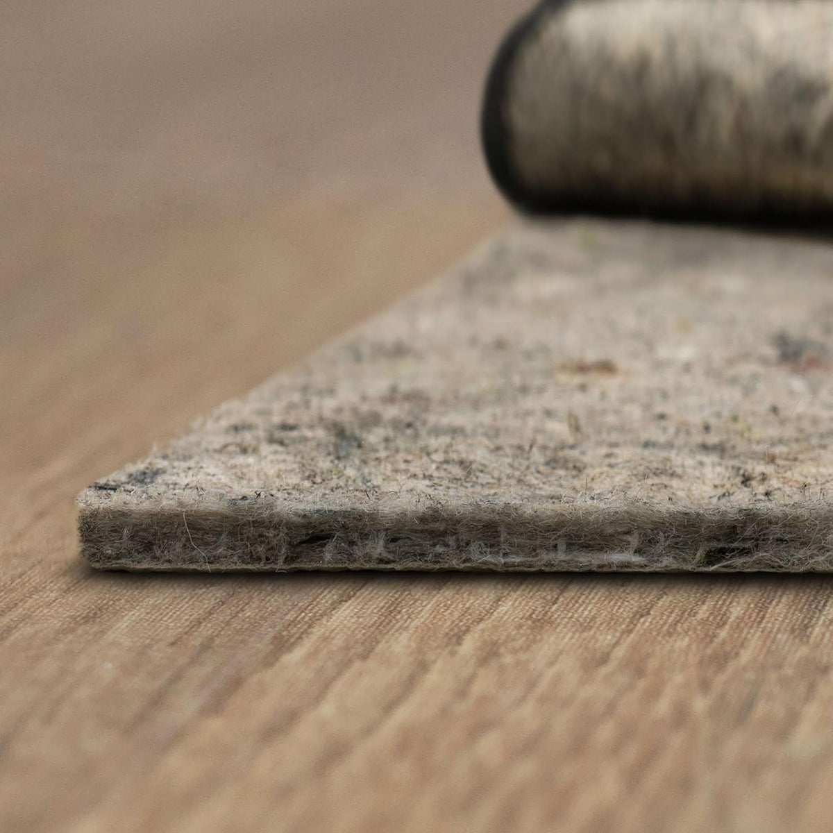 Close-up side profile of felt rug pad showing recycled fiber cushion on a hardwood floor