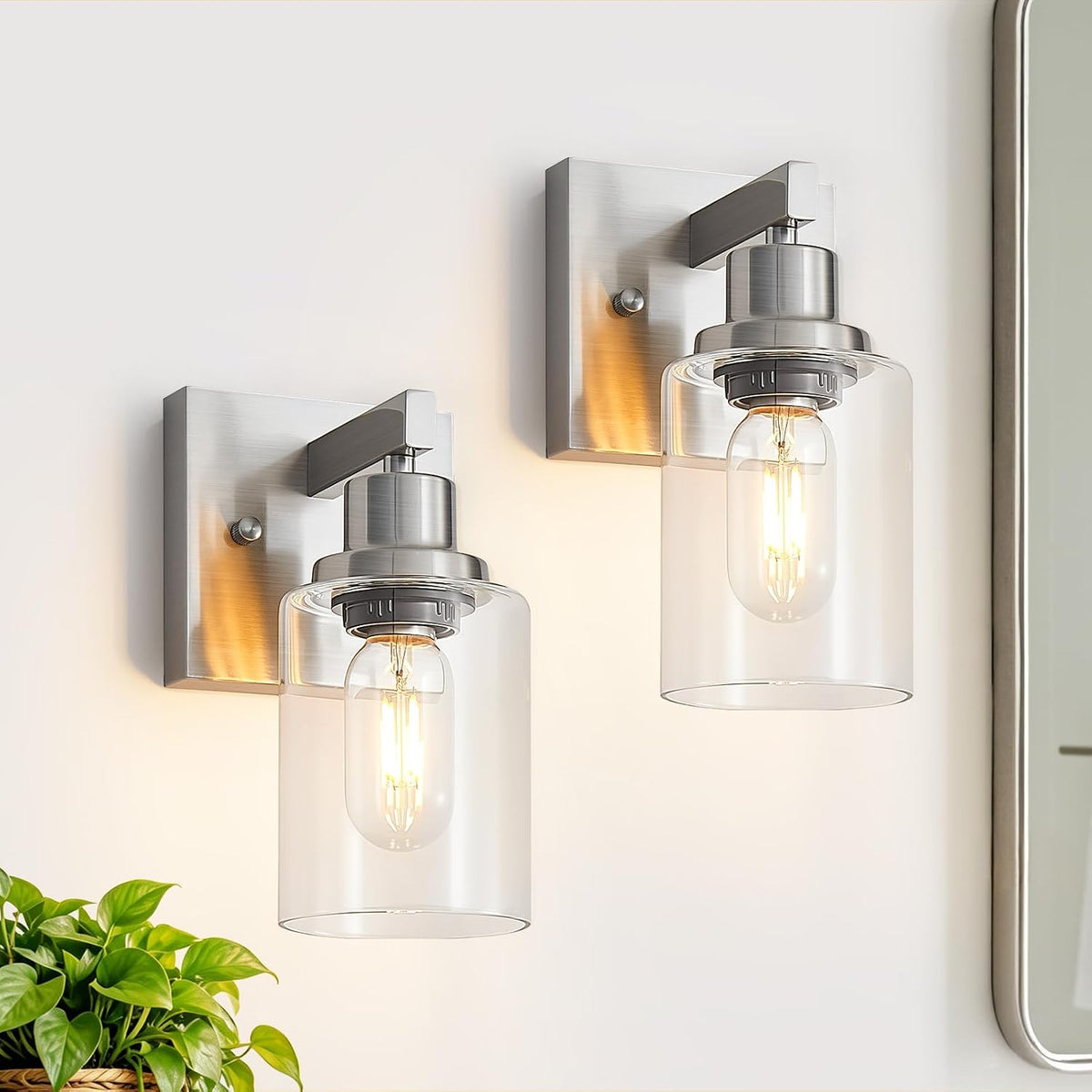 Close-up of two brushed metal wall sconces with clear glass cylinder shades and lit bulbs