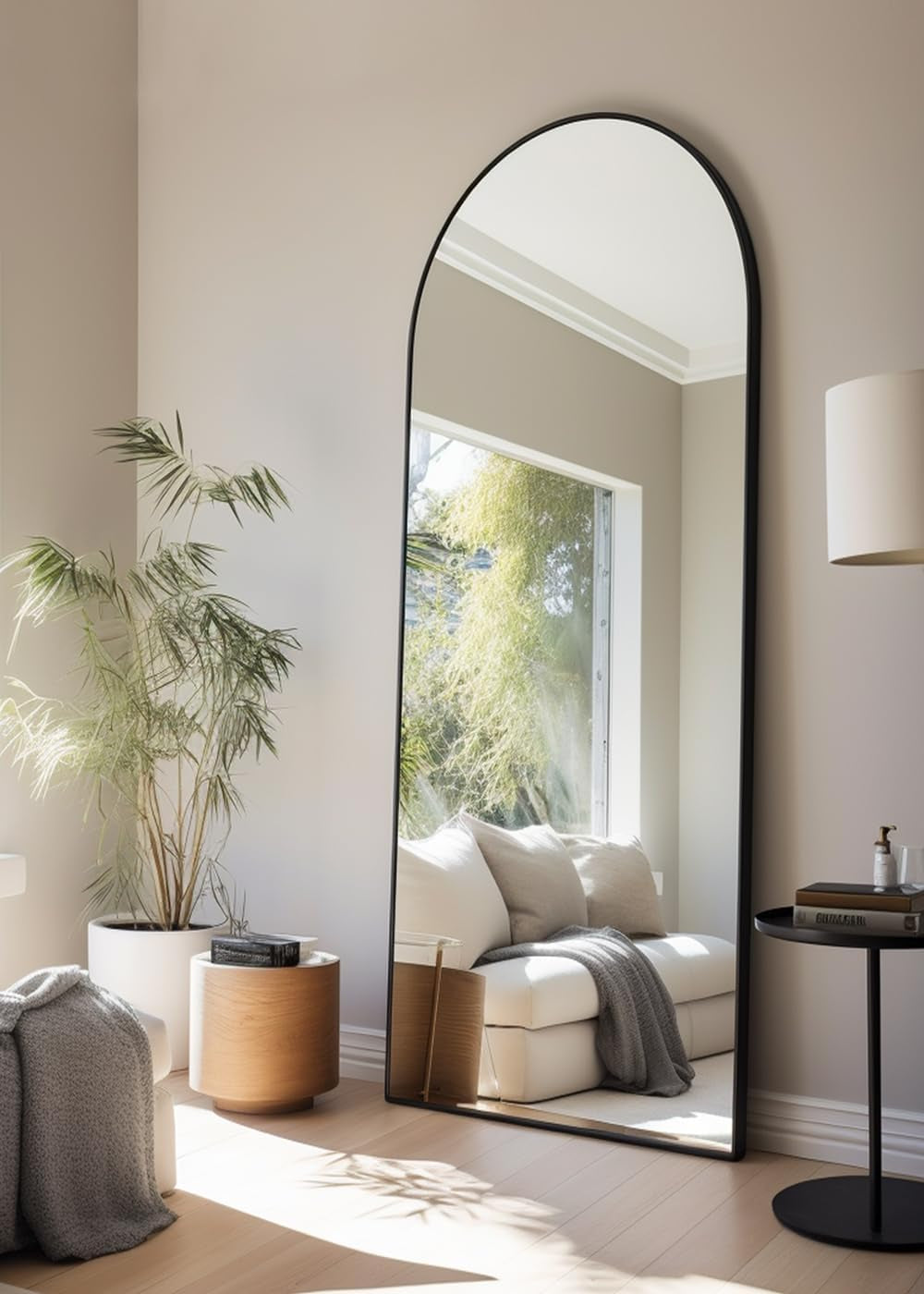 Tall arched floor mirror with a black frame leaning against a wall reflecting a sofa and window.