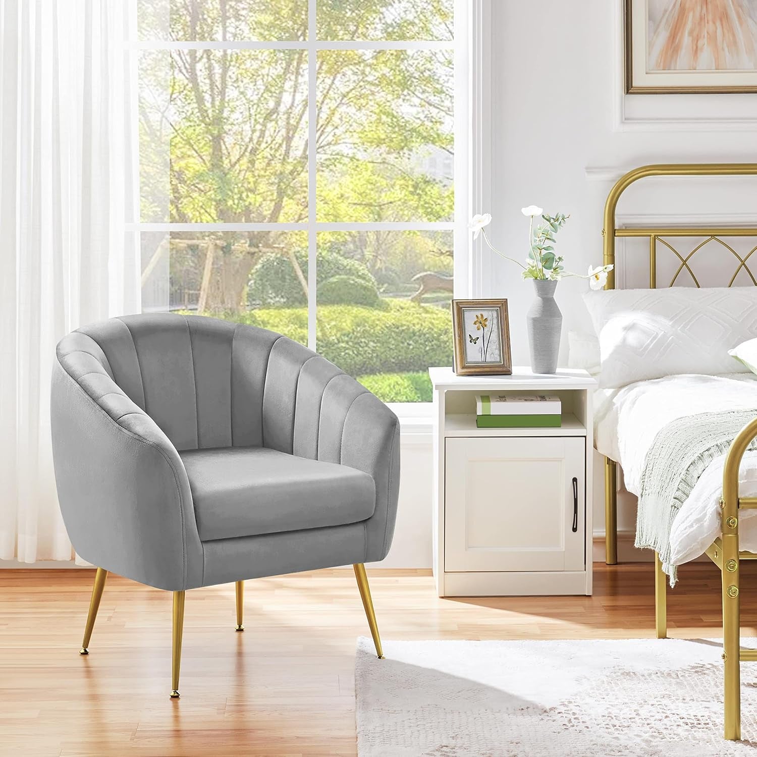 Single gray barrel chair with gold legs beside a white nightstand and bed in a sunlit bedroom.