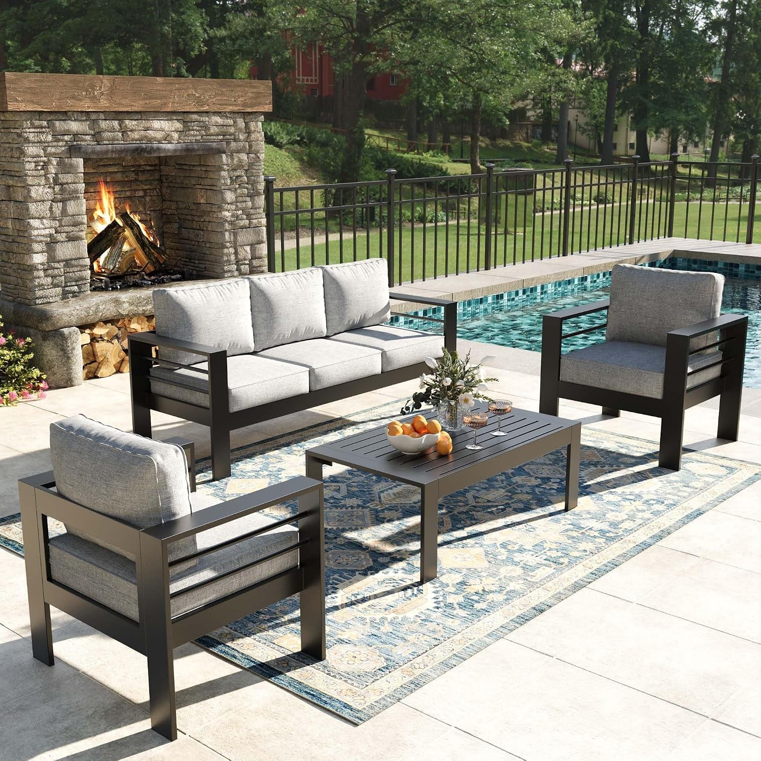 Outdoor patio set with dark metal frames and light gray cushions beside a pool and stone fireplace.
