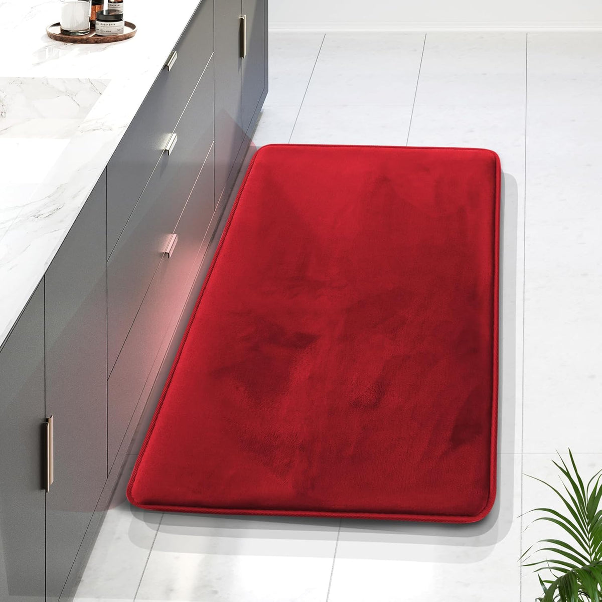 Long red rectangular memory-foam bath runner placed beside a gray vanity on white tile.