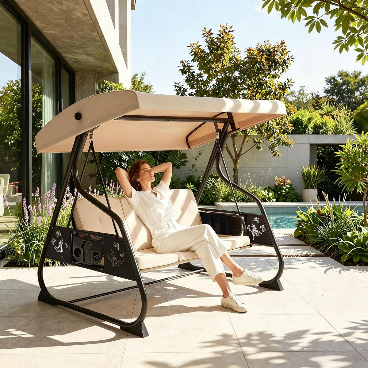Beige-cushioned porch swing on a tiled patio by a pool, a woman reclining under the adjustable canopy.