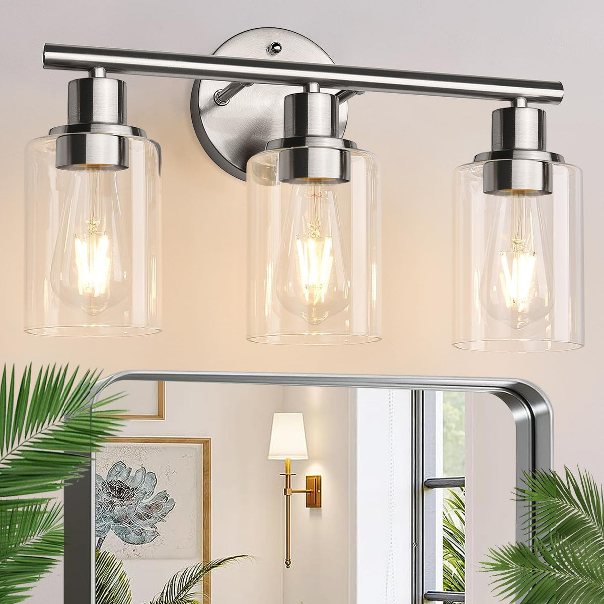 Three-light brushed silver vanity light with clear cylindrical glass shades above a mirror