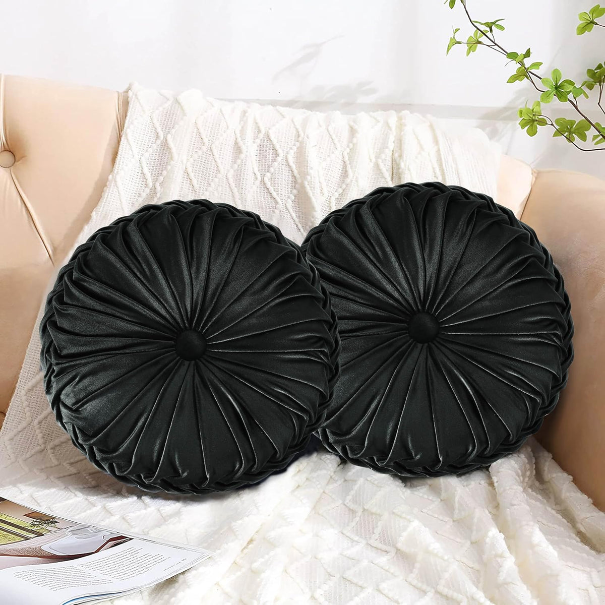 Two black round ruched pillows with button centers arranged on a pale sofa and textured white throw.
