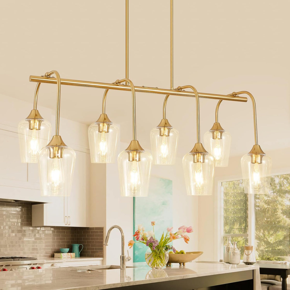 Gold linear multi-light fixture installed above a kitchen island with flowers and faucet below.