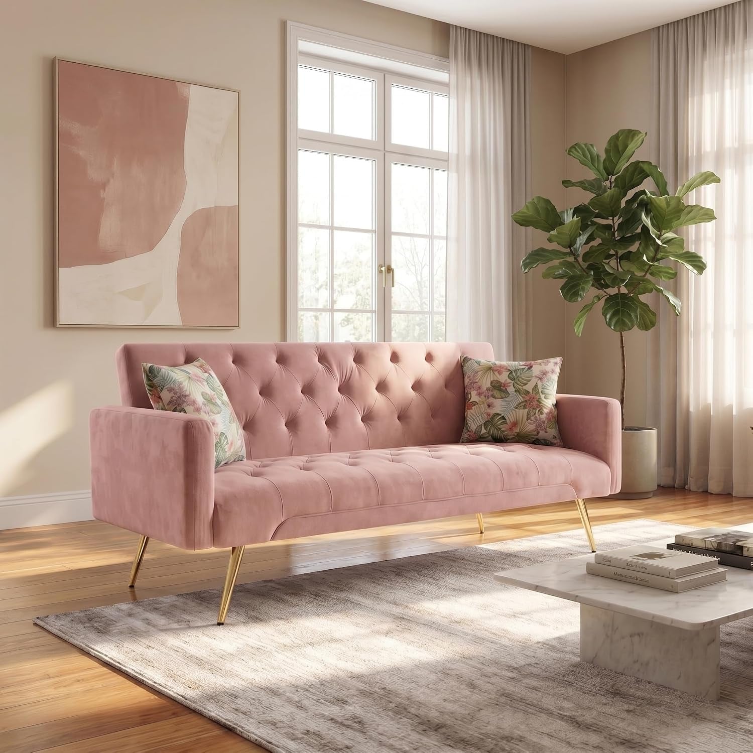 Staged pink tufted velvet sofa with gold legs and two floral throw pillows in a sunlit living room.