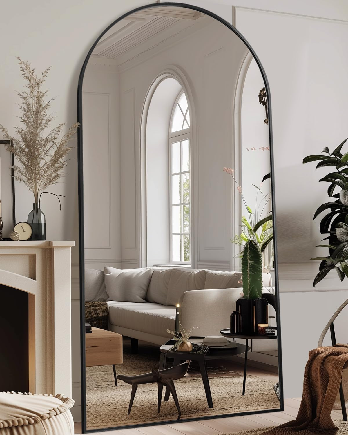 Tall arched full-length mirror with slim black frame leaning against a living room wall.
