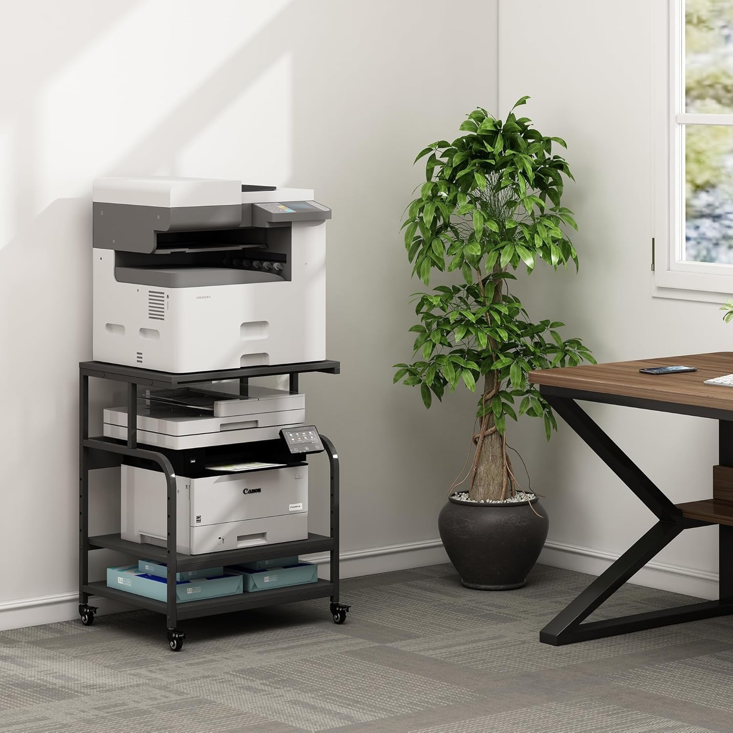 Black 3-tier printer stand in an office setting with stacked printers and a potted plant near a desk