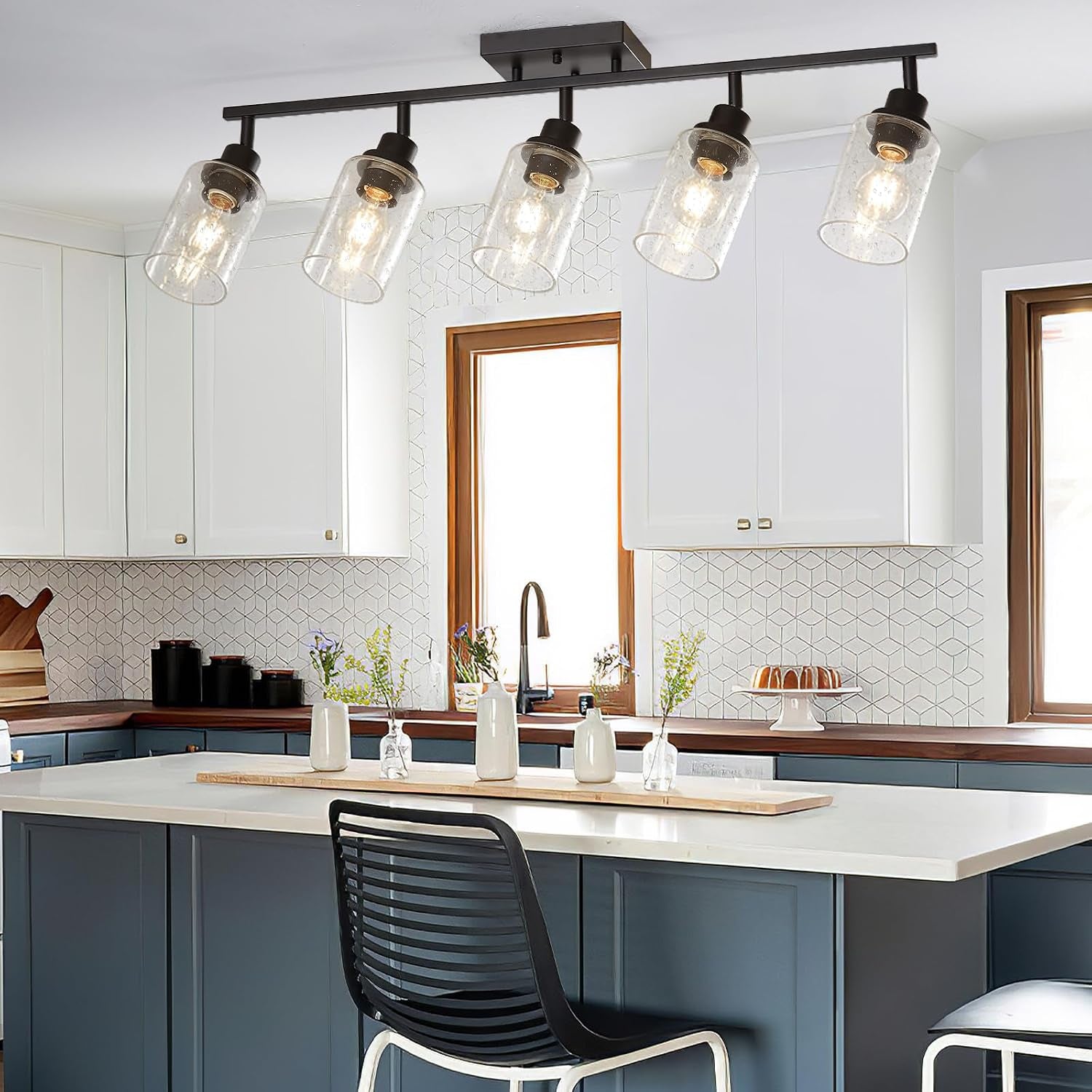 Matte black track lighting above a blue island with a black slatted chair and pendant-style seeded glass shades.