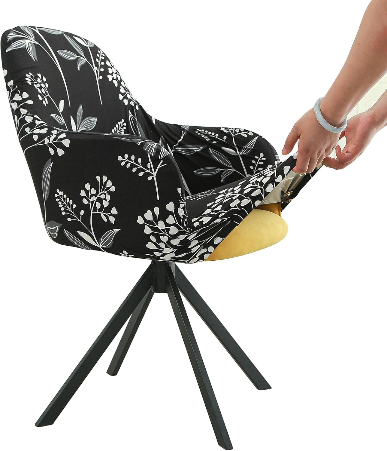 Side view of a black chair cover with white botanical print being eased over an armchair by two hands.