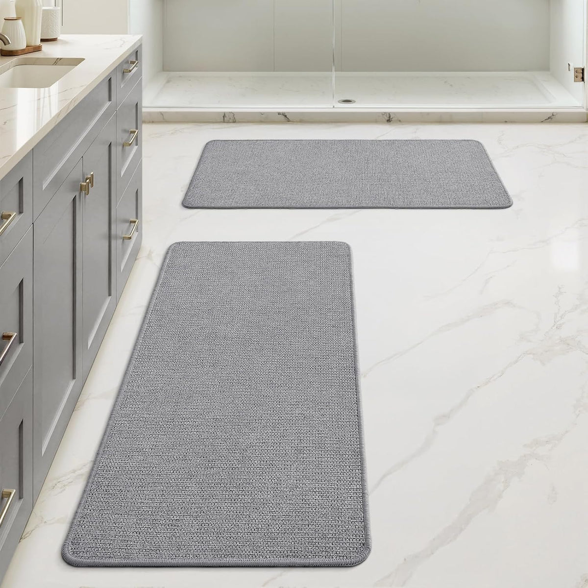 Bathroom scene with two rectangular textured gray floor mats placed near shower and vanity.
