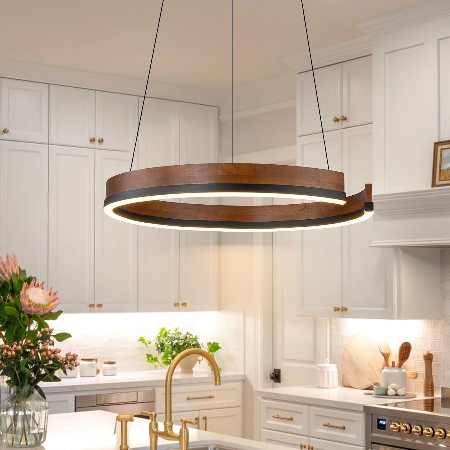 Angled view of a suspended walnut wood ring pendant illuminating a white kitchen island and gold faucet.