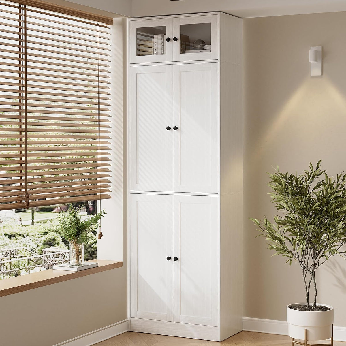 Tall white 7-tier bookcase with closed doors tucked in a corner next to a window and potted plant.