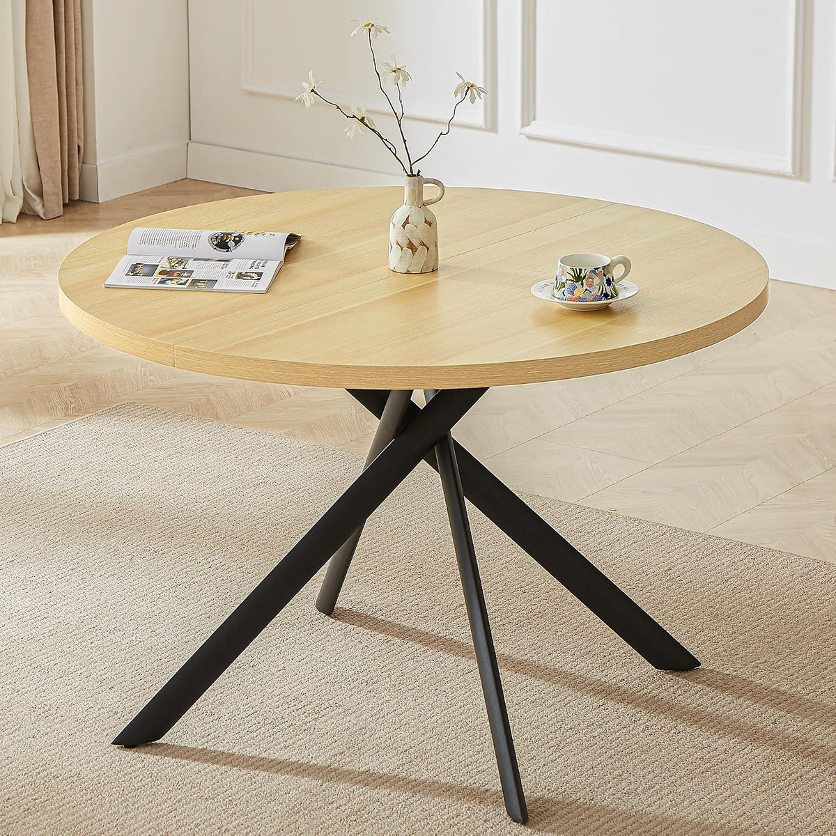 Close-up of a round light-wood tabletop and black crossed metal legs on a neutral rug.