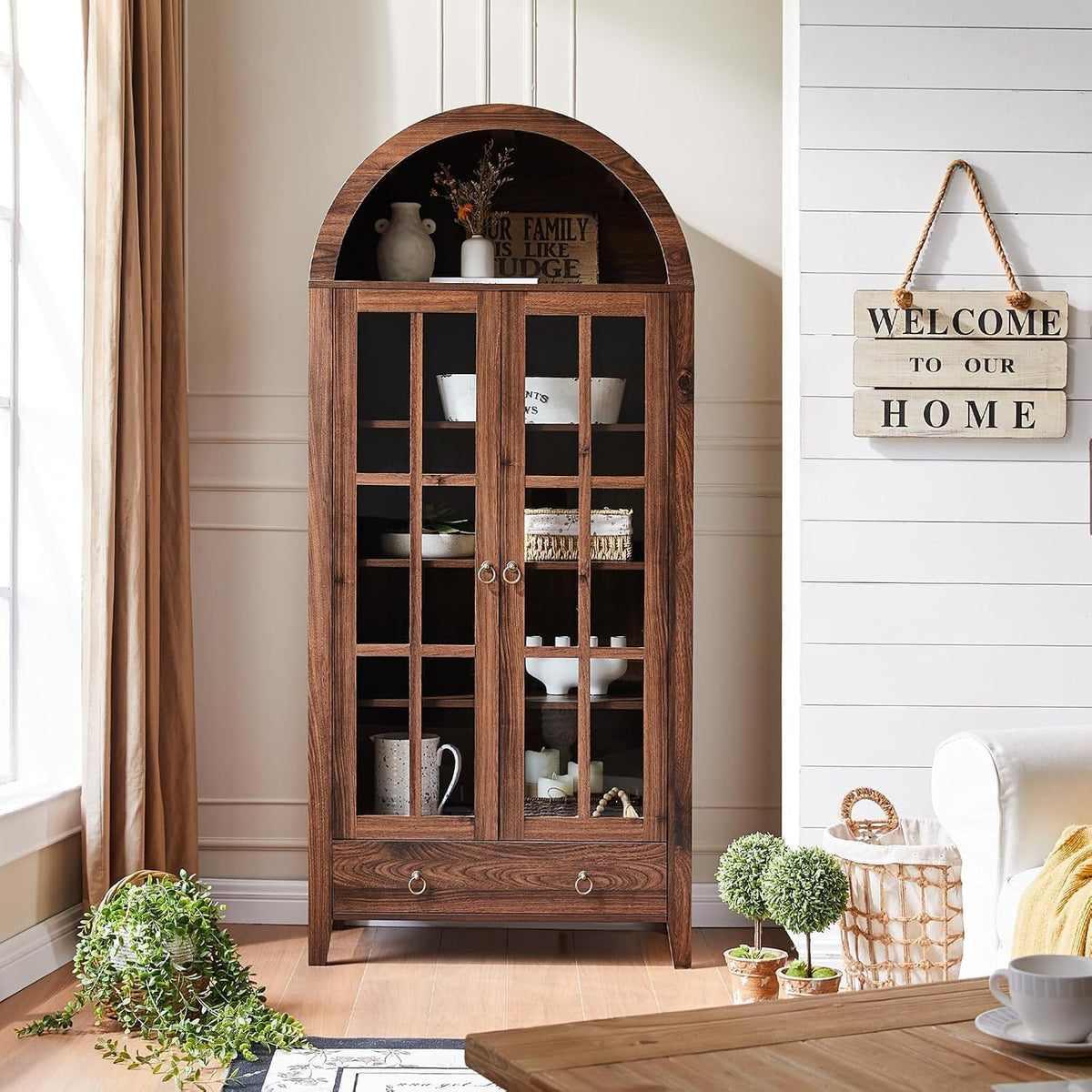 Brown arched glass-door cabinet bookshelf styled in a bright living room