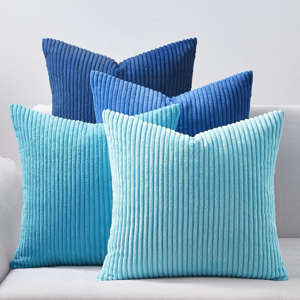 Four corduroy ribbed pillows in blue tones layered on a pale sofa