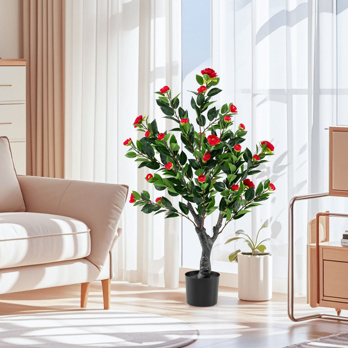 Red-blossomed artificial camellia tree in a black pot beside a pale sofa