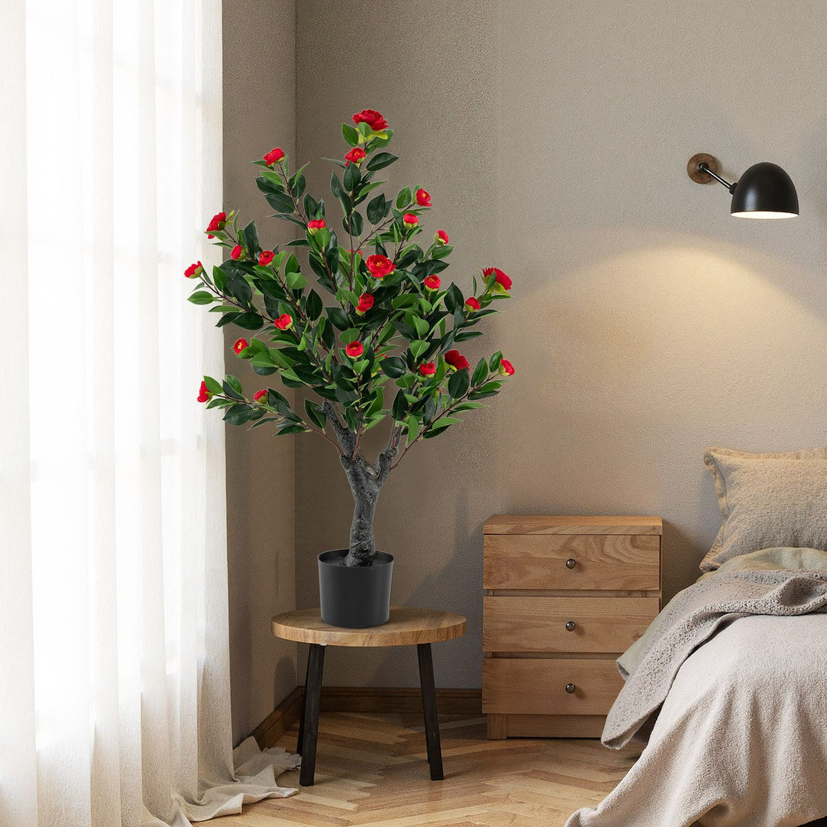 Red-blossomed camellia tree in a black pot beside a bed and wooden table