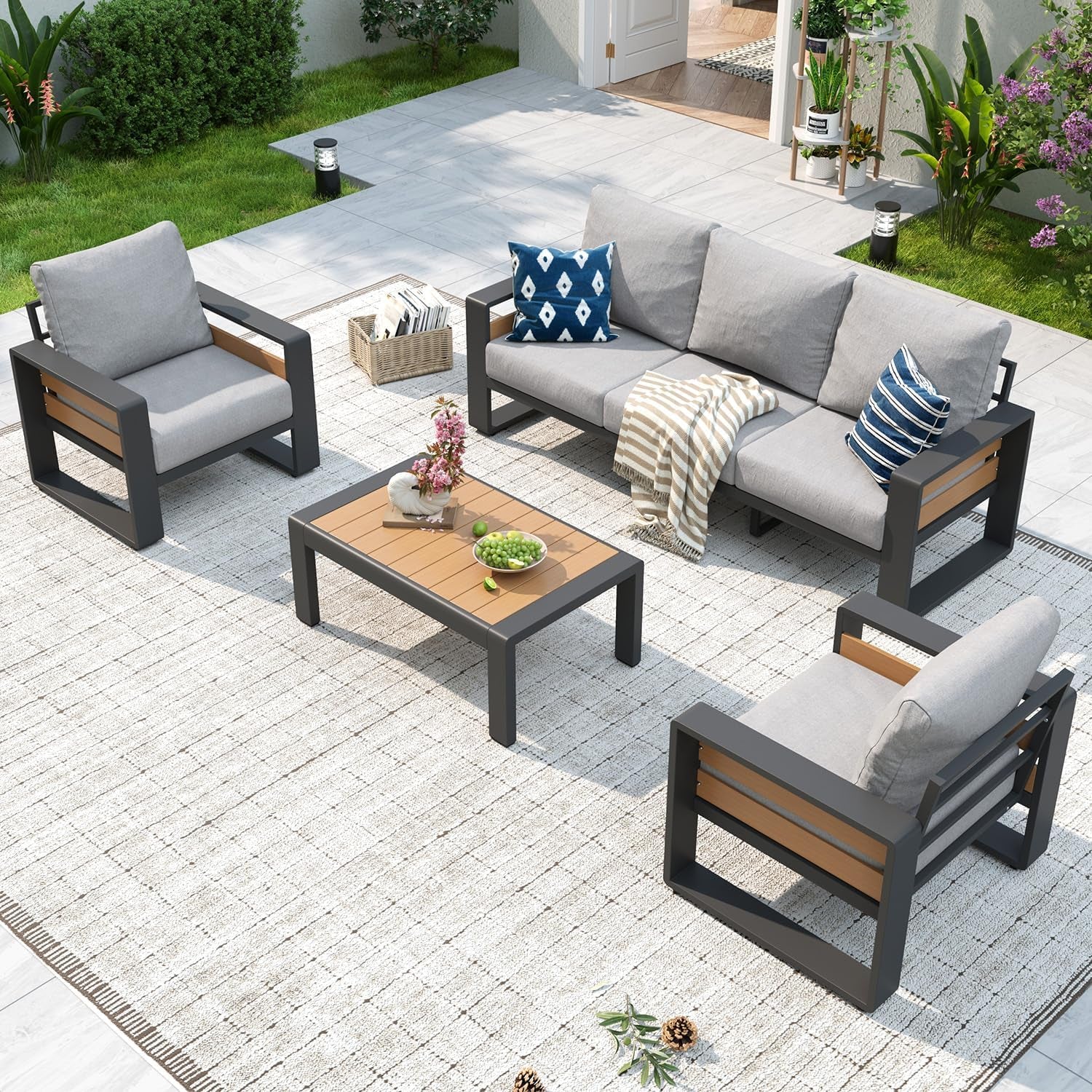 Patio set staged outdoors with dark gray frames and light gray cushions, coffee table and decorative pillows.