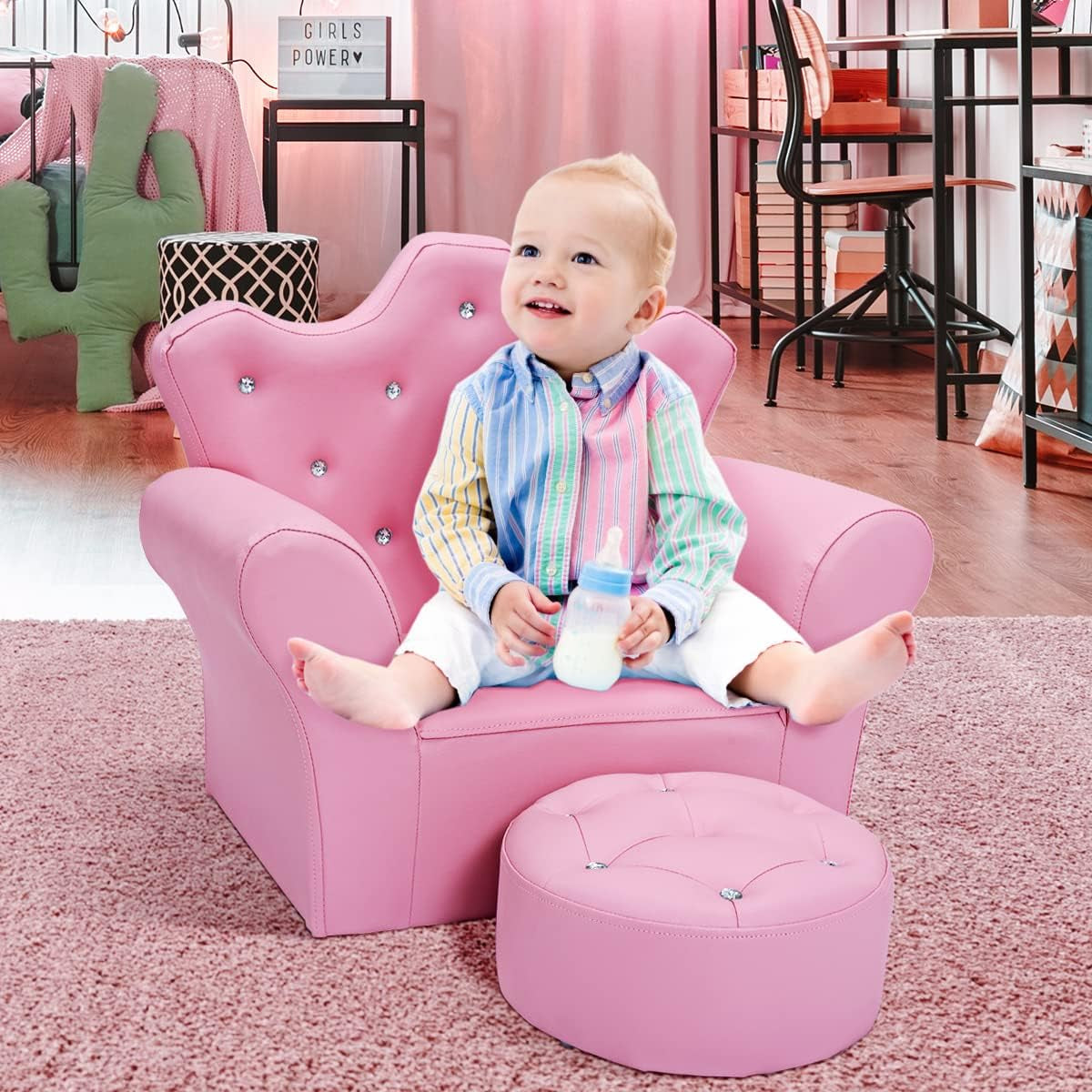 Child sitting on pink toddler chair with ottoman in a bedroom setting, toys and furniture in background